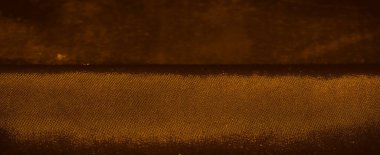 Sıcak kahverengi ve turuncu tonlarda desenli dokulu bir yüzeye yakın çekim. Bu ipek, küçük dairelerden oluşan ince bir şebeke, organik gibi hissettiren karmaşık bir dizayn yaratıyor..