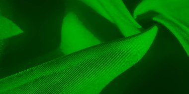 Yumuşak kıvrımlara ve aydınlık ve karanlığın keskin kesişimlerine odaklanan yeşil bir kumaş. Kumaş dokusu ve pürüzsüzlüğü, gölgenin çarpıcı kontrastı ile gelişir.