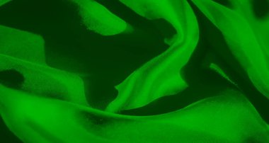 Pürüzsüz yeşil bir kumaş, gölgelerin ve ışığın yüzeyde oynadığı yakın planda sergilenir. Kumaşın ipeksi, akışkan dokusu dinamik ama yumuşak bir etki yaratır..