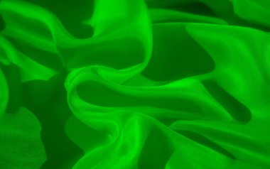 Fotoğrafta canlı yeşille çekilmiş pürüzsüz, akışkan bir kumaş var. Katlar ve katlar, dokuyu geliştiren yumuşak gölgelerle dinamik ve soyut bir etki yaratır..