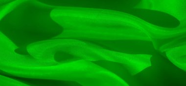 Karmaşık kıvrımlı yeşil saten kumaşın yakın çekim görüntüsü. Görüntü, materyalin pürüzsüzlüğünü ve parıltısını vurgular. Lüks ve soyut bir his yaratır. Yumuşak gölgeler kıvrımlarını yükseltir..