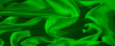 Görüntü, yüzeyindeki ışık ve gölgenin etkileşimini vurgulayan pürüzsüz yeşil bir kumaşı tasvir ediyor. Kumaşın kıvrımları lüks hissettiren zarif, akıcı bir kompozisyon yaratır.