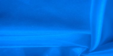 Yumuşak ışıklandırmalı, pürüzsüz, mavi bir kumaşın yakın plan çekimi ince dokuları vurguluyor. Bu kıvrımlar hem dinamik hem de sakinleştirici olan bir sıvı, soyut desen oluşturuyor..