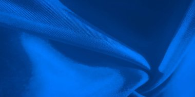 Yumuşak kıvrımları ve karmaşık dokusu olan pürüzsüz, mavi bir kumaşın çarpıcı yakın çekimi. Işık ve gölge, kumaşların akıcılığını ve yumuşaklığını vurgulayan bir derinlik ve hareket hissi yaratır.