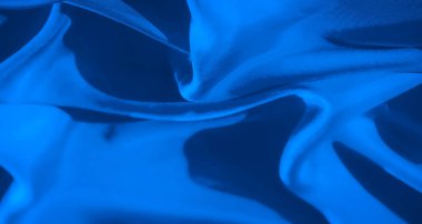 Bu görüntü, yumuşak ışıkla aydınlatılmış parlak mavi bir kumaşın karmaşık kıvrımlarını ve dokusunu yakalar. Tekstilin pürüzsüz, akıcı yüzeyi dinamik çizgiler ve ince gölgeler yaratır..