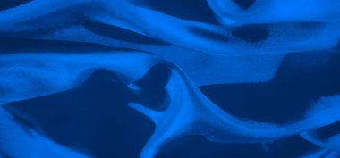 Yakın planda pürüzsüz mavi bir kumaş, soyut, dinamik, akışkan çizgiler ve ince eğriler oluşturur. Yumuşak kıvrımlar ve doku minimalist ve modern bir görsel deneyim sağlıyor..