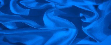 Pürüzsüz ve parlak mavi kumaşların karmaşık dokularını gösteren detaylı bir makro çekim. Görüntü, kumaşın kıvrımlarını ve kıvrımlarını vurgular, akıcı ve dinamik bir etki yaratır..