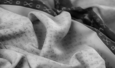 Açık gri kumaş, tekrarlanan üzengimsi bir dizaynla süslenmiş, doğal gölgeler yaratmak için hafifçe katlanmış. Yumuşak, minimalist bir estetik sunar..