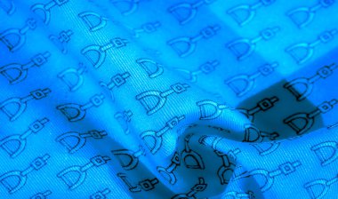 Soyut, dinamik düzende siyah üzengimsi desenli mavi kumaş. Tekstil, kıvrımlar ve doğal dokularla vurgulanmış, tekrarlayan binicilikten esinlenilmiş bir tasarıma sahip..