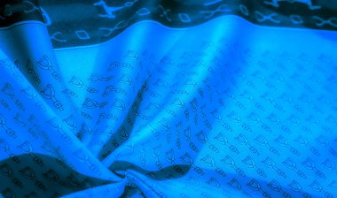 Soyut, dinamik düzende siyah üzengimsi desenli mavi kumaş. Tekstil, kıvrımlar ve doğal dokularla vurgulanmış, tekrarlayan binicilikten esinlenilmiş bir tasarıma sahip..