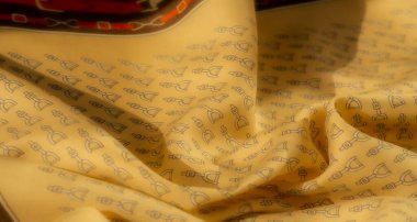 Sarı bir kumaşın yakın plan çekimi üzengiye benzer detaylı bir desen içerir. Kumaşın yumuşak kıvrımları ve karmaşık tasarımı binicilik ve tekstil için mükemmel ama zarif bir doku yaratır.