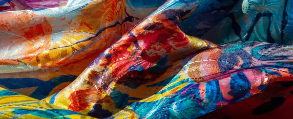 Mavi, pembe ve sarı lekeli parlak, soyut bir tekstil manzarası. Parlak bitiş, kumaşın zengin dokularını ve kıvrımlarını vurgular.