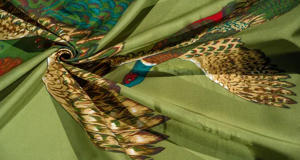 Kafası ve vücudunun bir kısmı canlı kırmızılar, yeşiller ve maviler içinde katlanmış kumaş arka planda sergilenen uçan bir sülünün yakın çekimi..