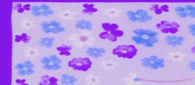 Mavi ve mor çiçek motiflerinin karışımı yumuşak mor gölgeli bir kumaşın bulanık ayrıntıları. Çiçekler ince bir akış için narin pembe saplarla birbirine bağlanarak yüzeyin her tarafına dağılmış..