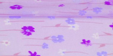 Yumuşak mor bir kumaşın bulanık görüntüsü. Mavi, beyaz ve mor çiçekli narin bir deseni var. Rüya gibi, soyut bir doku yaratıyor..
