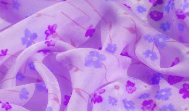 Karmaşık çiçek desenli, mor ve mavi çiçeklerin bulunduğu yumuşak lavanta kumaşın bulanık görüntüsü. Yumuşak kıvrımlar ve pürüzsüz dokular sakin ve rahatlatıcı bir atmosfer sağlar..