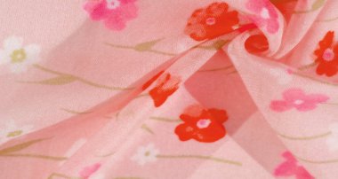 Yumuşak, akıcı bir kumaşa basılmış canlı kırmızı ve pembe çiçekleri olan pembe çiçekli bir kumaşın bulanık görüntüsü. Kumaşın kıvrımları ince gölgeler ve pürüzsüz dokularla dinamik bir görsel efekt yaratır..