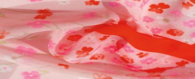 Pembe kumaşın yumuşak kıvrımlarını gösteren bulanık görüntü canlı çiçek desenleri ve kırmızı çizgilerle süslenmiş. Renklerin ve dokuların birleşimi soyut ama zarif bir görsel deneyim yaratır..