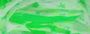 Yeşil ve beyaz çiçeklerin karışımı çiçek izleriyle kaplı canlı yeşil bir kumaşın bulanıklığı. Kumaşların hafif dokusu ve akışkan doğası canlandırıcı, doğadan esinlenilmiş bir arka plan sağlar..