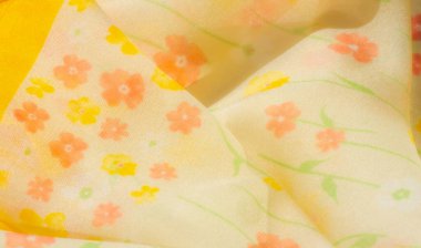 Yumuşak pembe ve turuncu çiçekli narin sarı çiçekli bir kumaşın bulanıklığı. Hafif, havadar bir arkaplana yayılmış. Akan kumaş yumuşak kıvrımlar oluşturur ve canlı deseni güçlendirir..