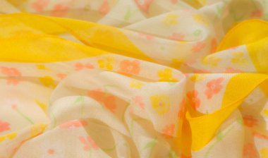 Beyaz, turuncu, sarı ve yeşil renklerinde pastel çiçek desenleriyle süslenmiş sarı kumaş bulanıklığı. Hassas kıvrımlar hareket ve doku ekler, kumaşların yumuşak ve havadar görünmesini sağlar..