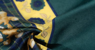 Sarı çiçek desenleriyle süslenmiş yeşil ve mavi ekose kumaşın yumuşak kıvrımlarını bulanıklaştır. Kumaştaki yumuşak kıvrımlar ve gölgeler yumuşak metnini vurgular.