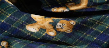 Neşeli oyuncak ayılarla süslenmiş ve canlı sarı çiçek desenleriyle çevrili yeşil ekose kumaş bulanıklığı. Karşıt dokular bir dinamik yaratır.