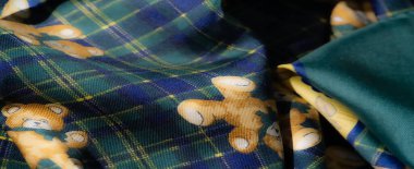 Karmaşık çiçek desenli yeşil ve sarı kumaş ve ekoseli ayıcık desenli. Parlak ve dünyevi tonların karşıtlığı dinamik ve oyuncu bir görsel etki yaratır..