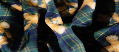 Renkli bir kumaş, ayıcıklı ve ekose bir arka planda çiçek desenleri var. Yeşil, sarı ve mavinin birleşimi eğlenceli ama samimi bir estetik katıyor..