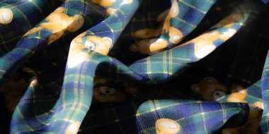 Renkli bir kumaş, ayıcıklı ve ekose bir arka planda çiçek desenleri var. Yeşil, sarı ve mavinin birleşimi eğlenceli ama samimi bir estetik katıyor..