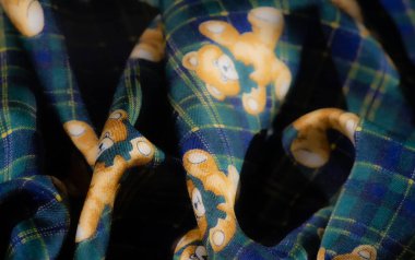 Mavi ve sarı çiçek desenlerinin hoş bir karışımını içeren kumaş bulanıklığı ekose yeşil arka planda oyuncak ayıların yanında. Yaratıcı projeler için eğlenceli ve kaprisli bir seçim.