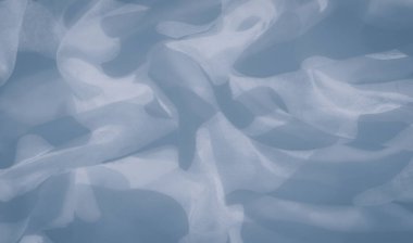 Üstüste binen desenli açık mavi kumaş bulanıklığı soyut şekiller yaratıyor. Yumuşak hareket ve narin kıvrımlar, gökyüzündeki yumuşak bulutları anımsatan sakin, akan bir atmosfer sunuyor..