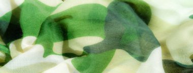 Canlı yeşil ve bej rengi kamuflaj desenli akışkan kumaş bulanıklığı. Kumaşın hafif dokusu havadar, dinamik bir hava katar. Bu da onu sanatsal ve yaratıcı tekstil arka planları için ideal kılar..