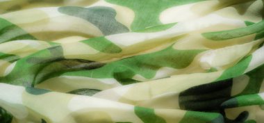 Dalgalı yeşil kamuflaj kumaşının bulanık ve soyut bir tasarımı var. Üst üste binen yeşil ve bej renkler, arka plan tasarımları veya giysi malzemeleri için ideal ince ve organik bir görünüm yaratıyor..