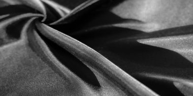 Görüntü, lüks siyah kumaşın yakın plan görüntüsü hassas kıvrımları ortaya çıkarır ve yumuşaklık ve parlaklığın soyut bir tasarımını yaratır. Kumaşların düz dokusu gölgeli alanlarla çelişiyor ve derinlik üretiyor.