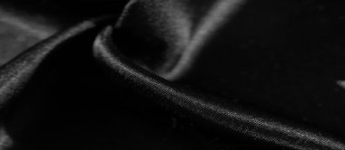 Siyah kumaş kıvrımları, parlak yüzeyinden yansıyan ışıkla soyut ve lüks bir desen oluşturur. Gölgelerin ve gölgelerin etkileşimi kumaşları yumuşatır.,