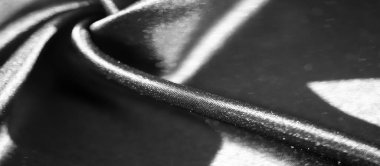 Görüntü. Karmaşık kıvrımları ve parlak yüzeyi olan siyah bir kumaş. Işığın ve gölgenin hassas etkileşimi maddenin lüks hissini arttırır ve sofistike bir ortam yaratır.