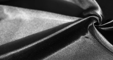 Zarif kıvrımlarda dönen parlak siyah kumaş bulanıklığı. İpeksi doku ve yansıtıcı yüzey, ışık ve gölgenin etkileşimiyle vurgulanan kumaşın lüks hissini arttırır..