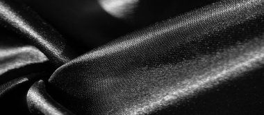 Parlak siyah kumaşın bulanık örtüsü, lüks dokusunu gözler önüne seriyor. Açık ve koyu renkli alanlar, kumaşın parlak ve akışkan özelliklerini vurguluyor.