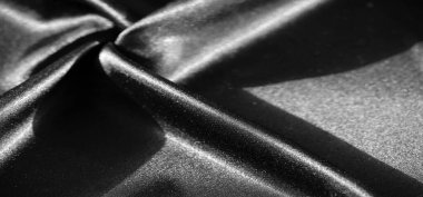 Pürüzsüz kıvrımları olan koyu, parlak kumaştan bir bulanıklık. Yansıtıcı yüzey ışık ve gölge arasındaki hassas etkileşimi vurgular, kumaşların yumuşak ve lüks dokusunu vurgular..