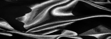 Görüntü. Yumuşak kıvrımlı, pürüzsüz, siyah saten kumaştan oluşan yakın plan bir çekim, röfleli ve gölgeli zarif bir doku yaratıyor. Kumaşın parıltısı lüks ve akıcı bir görünüm veriyor..