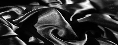 Bulanık siyah kumaş, pürüzsüz tabakalar halinde karmaşık bir şekilde katlanarak parlak ve yansıtıcı bir yüzey oluşturur. Koyu gölgeler ve ince gölgeler arasındaki zıtlık dokuyu ortaya çıkarır.