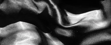 Görüntü. Yumuşak kıvrımlar ve kıvrımlar halinde akan zarif siyah saten kumaş, ışıktan titreyen bir efektle. Zengin dokusu bu soyut kumaş çekimine lüks ve tarz katıyor..