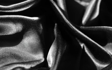 Zarif kıvrımlar ve kıvrımlarla örtülmüş parlak siyah saten kumaştan bir bulanıklık. Yüzeyinde hafif bir ışık var. Malzemenin zengin dokusu ve parlak parıltısı onu çarpıcı, zarif bir parça yapıyor..