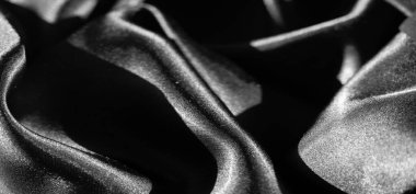 Karmaşık kıvrımlarda siyah saten kumaş bulanıklığı pürüzsüz dokusunu ve yansıtıcı parıltısını vurguluyor. Malzeme ışığı incelikle yakalıyor, gölgenin dramatik etkileşimini güçlendiriyor.