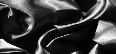 Akan kıvrımlar ve derin kıvrımlarda birbirine dolanmış siyah saten kumaş bulanıklığı parlak yüzeyini göstermek için yumuşak ışığı yansıtıyor. Doku ve derinlik lüks bir hareket hissi uyandırıyor.