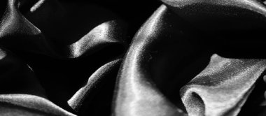 Karmaşık kıvrımlarda siyah saten kumaş bulanıklığı pürüzsüz dokusunu ve yansıtıcı parıltısını vurguluyor. Malzeme ışığı incelikle yakalıyor, gölgenin dramatik etkileşimini güçlendiriyor.