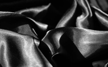 Işıl ışıl kıvrılan kıvrımlarıyla ışık saçan lüks siyah kumaş bulanıklığı. Pürüzsüz, parlak doku zarif bir görünüş, zarif bir arkaplan ve dizayn için ideal bir yapı yaratır..