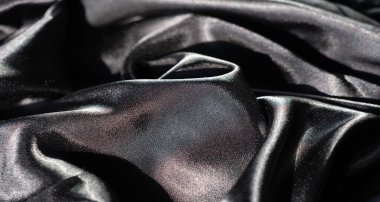 Kıvrımlı çizgileri ve kıvrımları olan parlak siyah bir kumaş. Pürüzsüz dokudaki ışık oyunu, kumaşların lüks kalitesini ve gölgelerle zıtlığını vurgular..