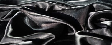 Kıvrımlı çizgileri ve kıvrımları olan parlak siyah bir kumaş. Pürüzsüz dokudaki ışık oyunu, kumaşların lüks kalitesini ve gölgelerle zıtlığını vurgular..